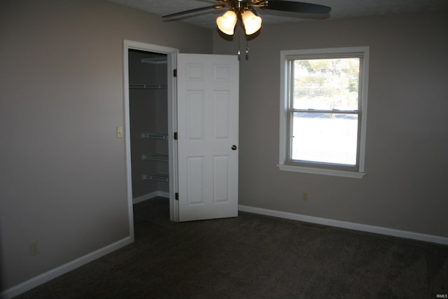 unfurnished bedroom with dark colored carpet, a walk in closet, baseboards, and multiple windows