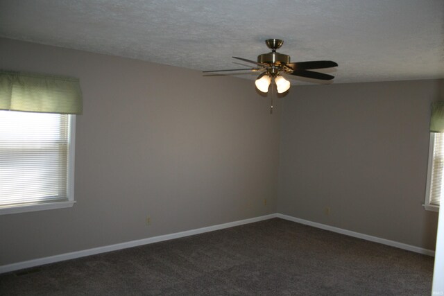 empty room with visible vents, a ceiling fan, a textured ceiling, dark carpet, and baseboards