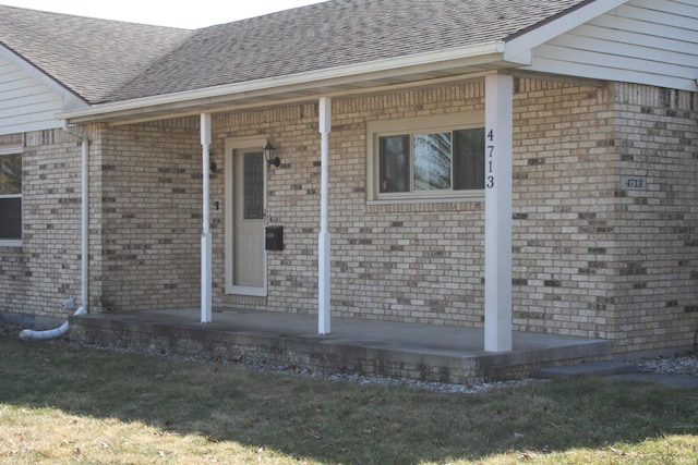 doorway to property with a yard, brick siding, and a shingled roof