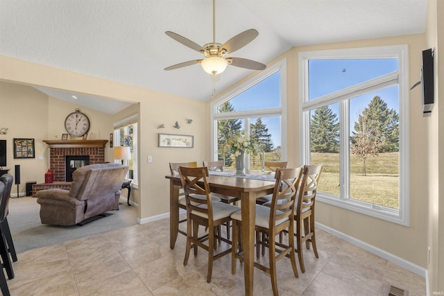 dining room featuring visible vents, baseboards, a brick fireplace, ceiling fan, and vaulted ceiling