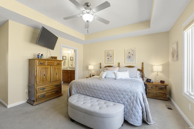 carpeted bedroom featuring visible vents, a raised ceiling, baseboards, and connected bathroom