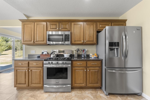 kitchen with brown cabinets, dark countertops, appliances with stainless steel finishes, and a textured ceiling