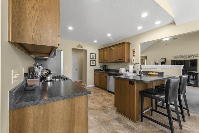 kitchen featuring a breakfast bar, a sink, dark countertops, appliances with stainless steel finishes, and a peninsula