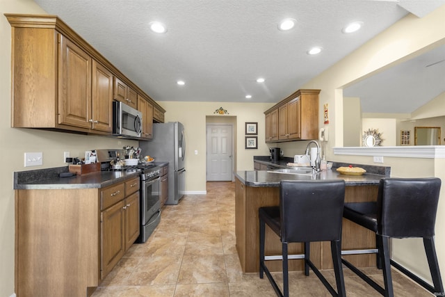 kitchen with a breakfast bar, a sink, dark countertops, appliances with stainless steel finishes, and a peninsula