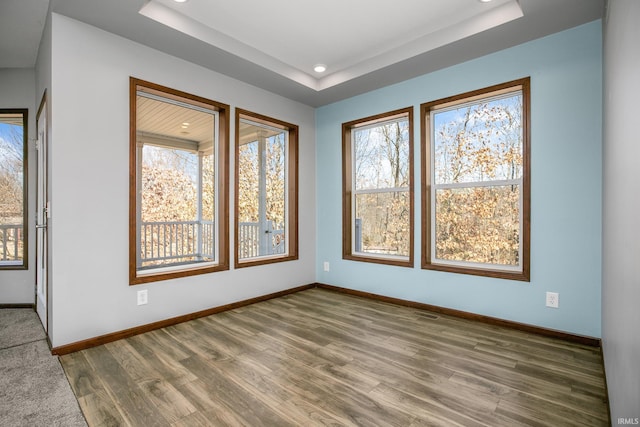 empty room with a raised ceiling, recessed lighting, wood finished floors, and baseboards