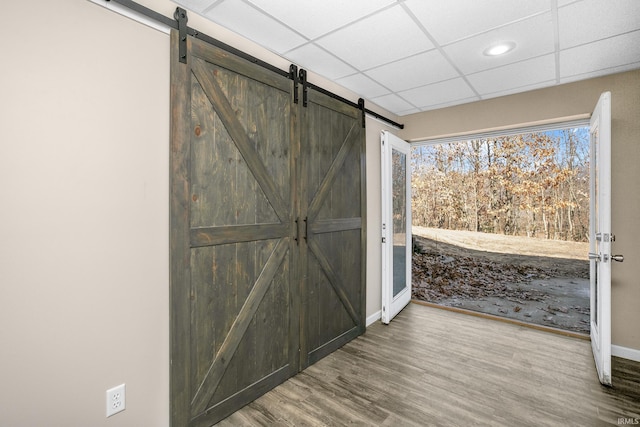 interior space with a barn door, wood finished floors, a paneled ceiling, and baseboards