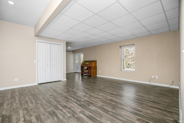 unfurnished living room featuring a paneled ceiling, baseboards, and dark wood-style flooring