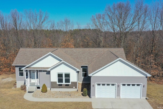 view of front of home featuring an attached garage, a view of trees, driveway, and roof with shingles