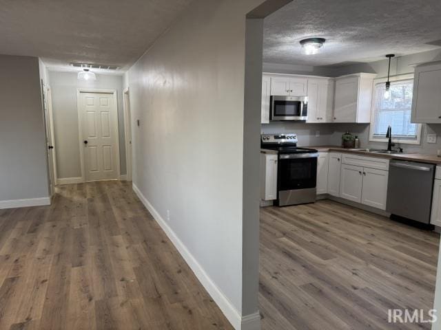 kitchen featuring wood finished floors, baseboards, a sink, stainless steel appliances, and a textured ceiling