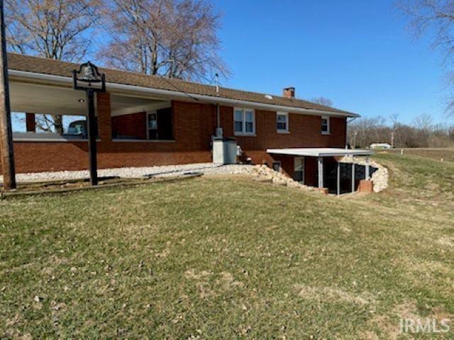 back of property featuring brick siding, a lawn, and a chimney