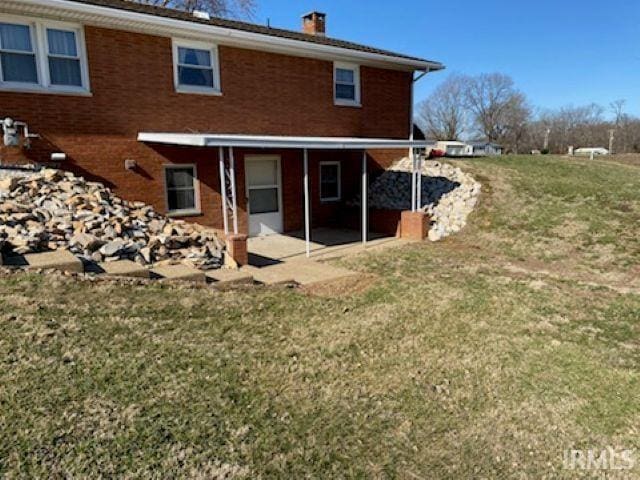 rear view of property featuring brick siding, a chimney, and a yard