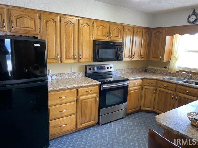 kitchen with brown cabinetry, black appliances, light countertops, and a sink