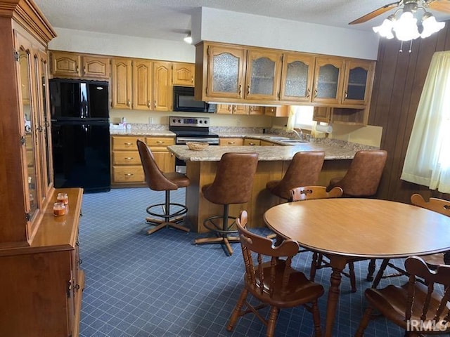 kitchen with a sink, glass insert cabinets, a peninsula, black appliances, and dark colored carpet