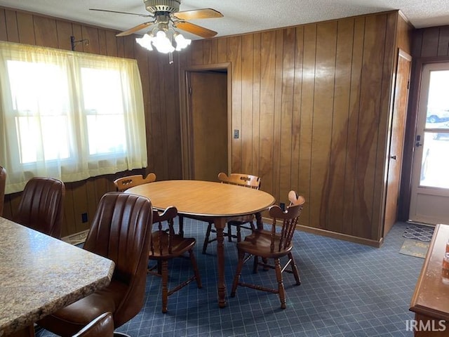 dining area with dark colored carpet, a textured ceiling, wood walls, and ceiling fan