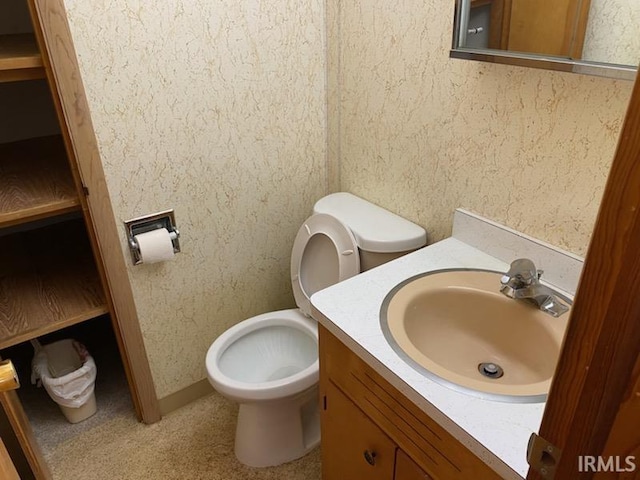 half bathroom with vanity, toilet, and wallpapered walls