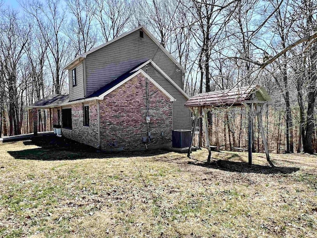 view of side of property featuring brick siding, central AC unit, and a lawn