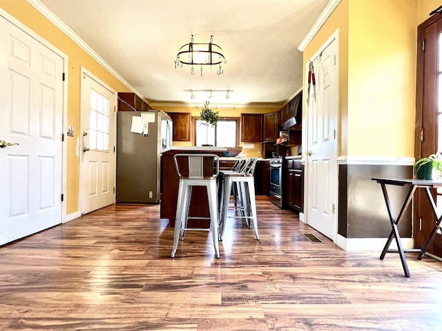 kitchen with wood finished floors, a kitchen island, ornamental molding, stainless steel appliances, and a kitchen breakfast bar