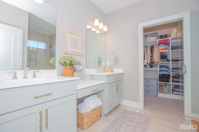 full bathroom featuring visible vents, a walk in closet, two vanities, a sink, and a shower