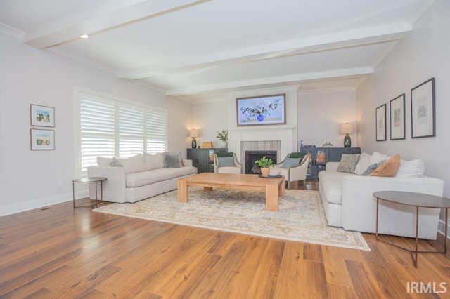 living room with beam ceiling, a tile fireplace, baseboards, and wood finished floors