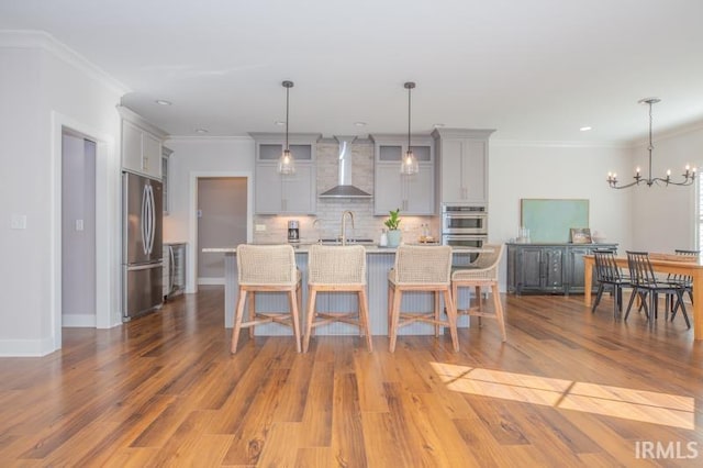 kitchen with a sink, gray cabinetry, light countertops, stainless steel appliances, and wall chimney range hood