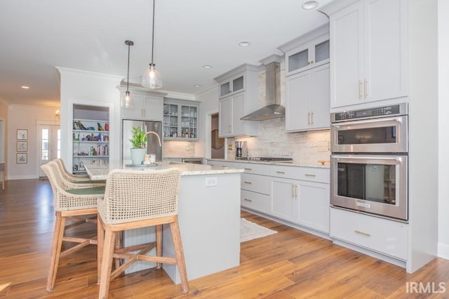 kitchen with ornamental molding, a kitchen bar, double oven, wall chimney exhaust hood, and backsplash