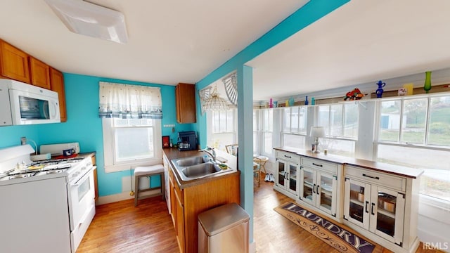 kitchen featuring a sink, light wood-type flooring, white appliances, and brown cabinets