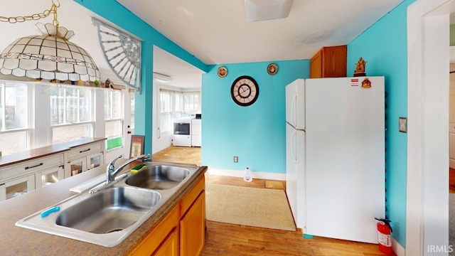 kitchen with brown cabinets, a sink, washing machine and dryer, freestanding refrigerator, and light wood finished floors