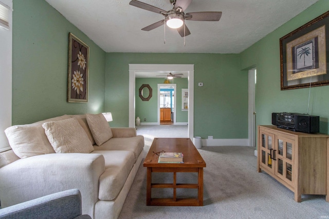 living area featuring baseboards, light carpet, a textured ceiling, and ceiling fan