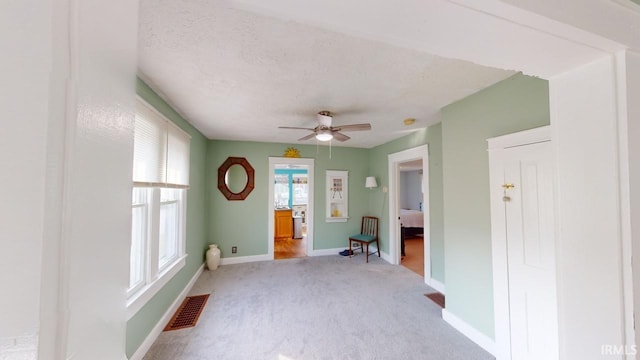 carpeted empty room featuring visible vents, a textured ceiling, baseboards, and a ceiling fan