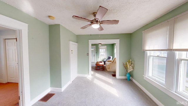 hallway featuring visible vents, baseboards, light colored carpet, and a textured ceiling