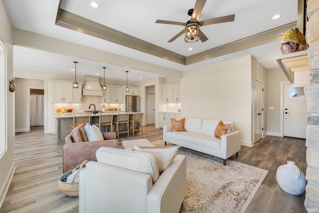 living area with baseboards, a tray ceiling, ornamental molding, recessed lighting, and light wood-style flooring