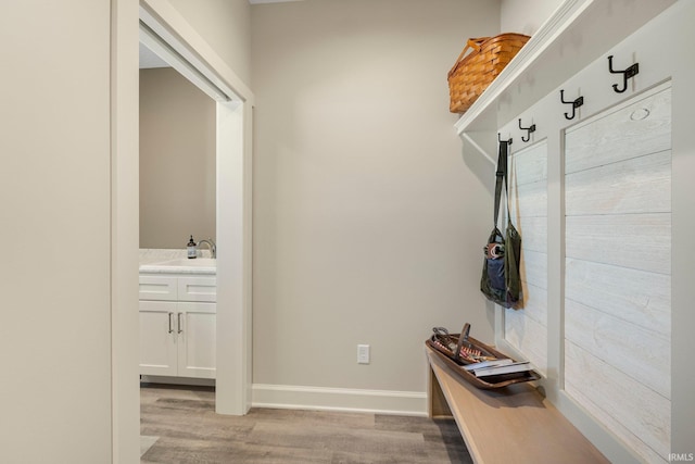 mudroom featuring light wood finished floors, baseboards, and a sink