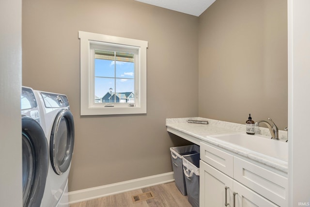 laundry room featuring a sink, washer and dryer, cabinet space, light wood finished floors, and baseboards