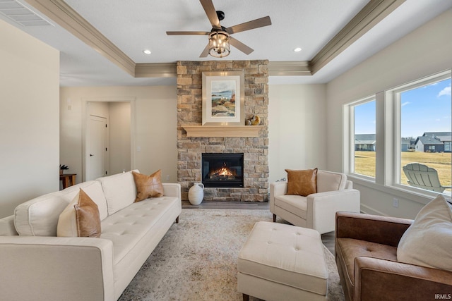 living room featuring visible vents, crown molding, a tray ceiling, a fireplace, and a ceiling fan