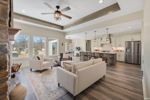 living room featuring dark wood-type flooring, a textured ceiling, crown molding, a raised ceiling, and ceiling fan