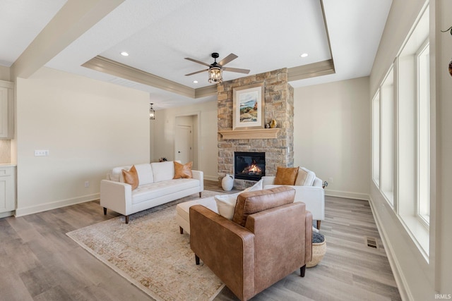 living room featuring visible vents, baseboards, a tray ceiling, a stone fireplace, and light wood-style floors