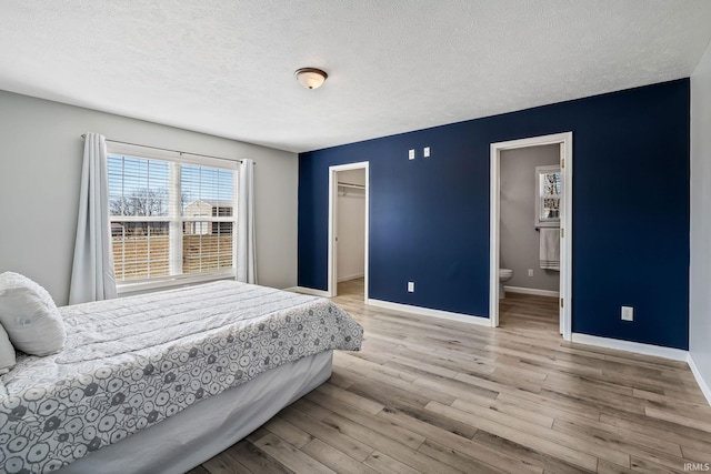 bedroom with a textured ceiling, ensuite bath, wood finished floors, baseboards, and a spacious closet