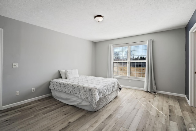 bedroom featuring a textured ceiling, baseboards, and wood finished floors