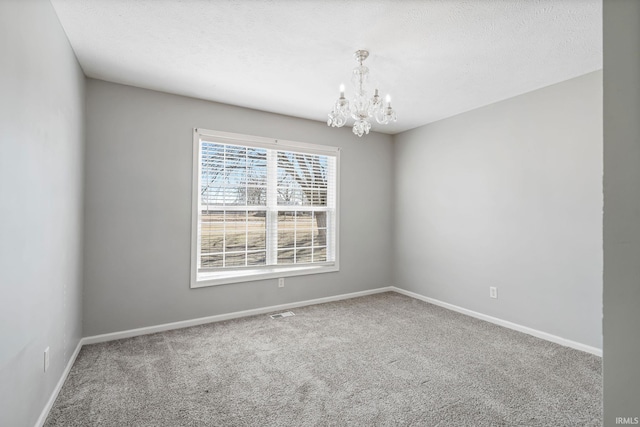 spare room featuring an inviting chandelier, carpet, baseboards, and a textured ceiling