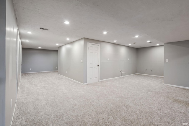 finished below grade area featuring baseboards, visible vents, recessed lighting, a textured ceiling, and light carpet