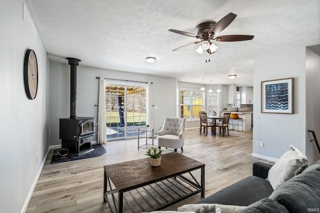 living room featuring ceiling fan, light wood-style flooring, a wood stove, and a textured ceiling