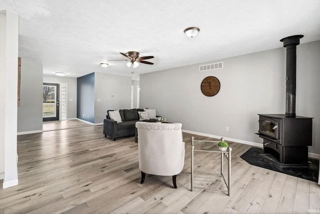 living area featuring visible vents, wood finished floors, baseboards, ceiling fan, and a wood stove