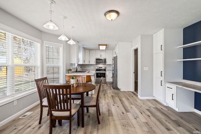 dining room with baseboards, light wood-style floors, visible vents, and a textured ceiling