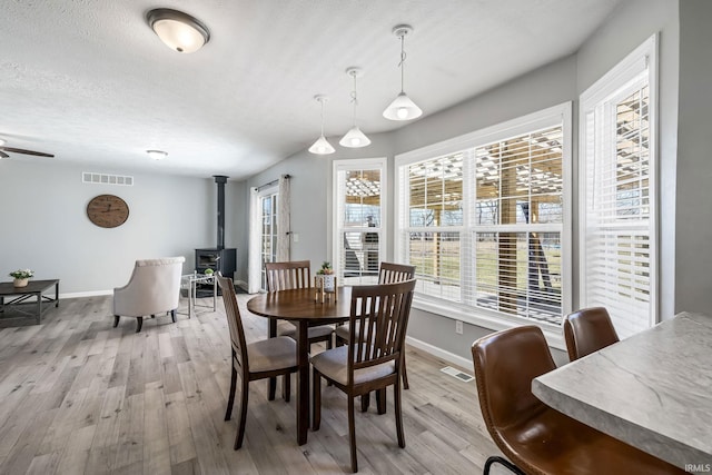 dining room with visible vents, a textured ceiling, a wood stove, and light wood finished floors