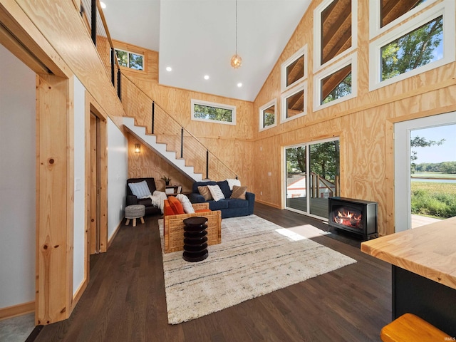 living area with stairway, wooden walls, baseboards, high vaulted ceiling, and dark wood finished floors