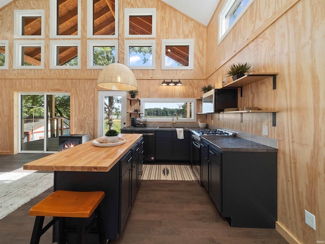 kitchen featuring butcher block countertops, open shelves, a center island, a breakfast bar area, and dark cabinets