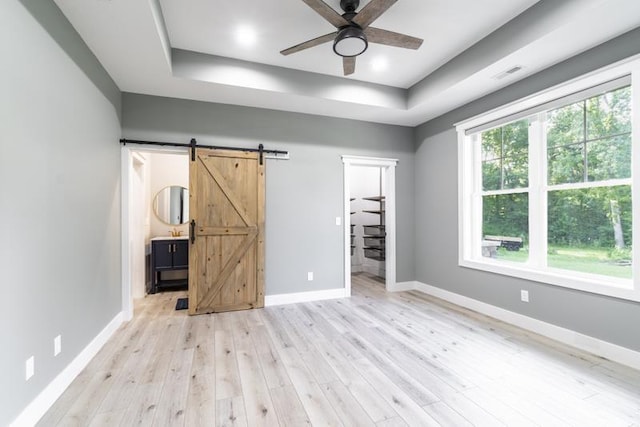 unfurnished bedroom featuring light wood finished floors, visible vents, a raised ceiling, and a barn door