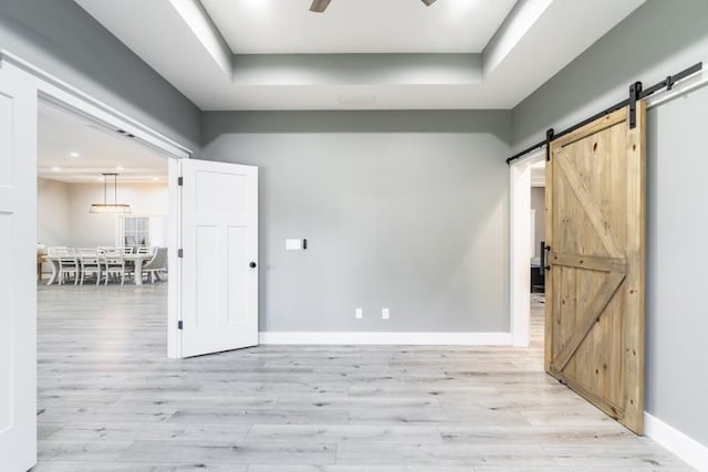 empty room with light wood finished floors, ceiling fan, baseboards, and a barn door