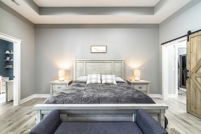 bedroom with a tray ceiling, baseboards, light wood-style floors, and a barn door