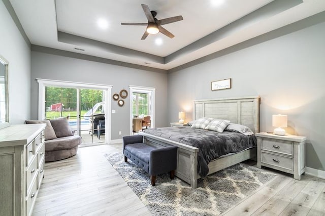 bedroom with baseboards, light wood-style floors, a tray ceiling, and access to outside